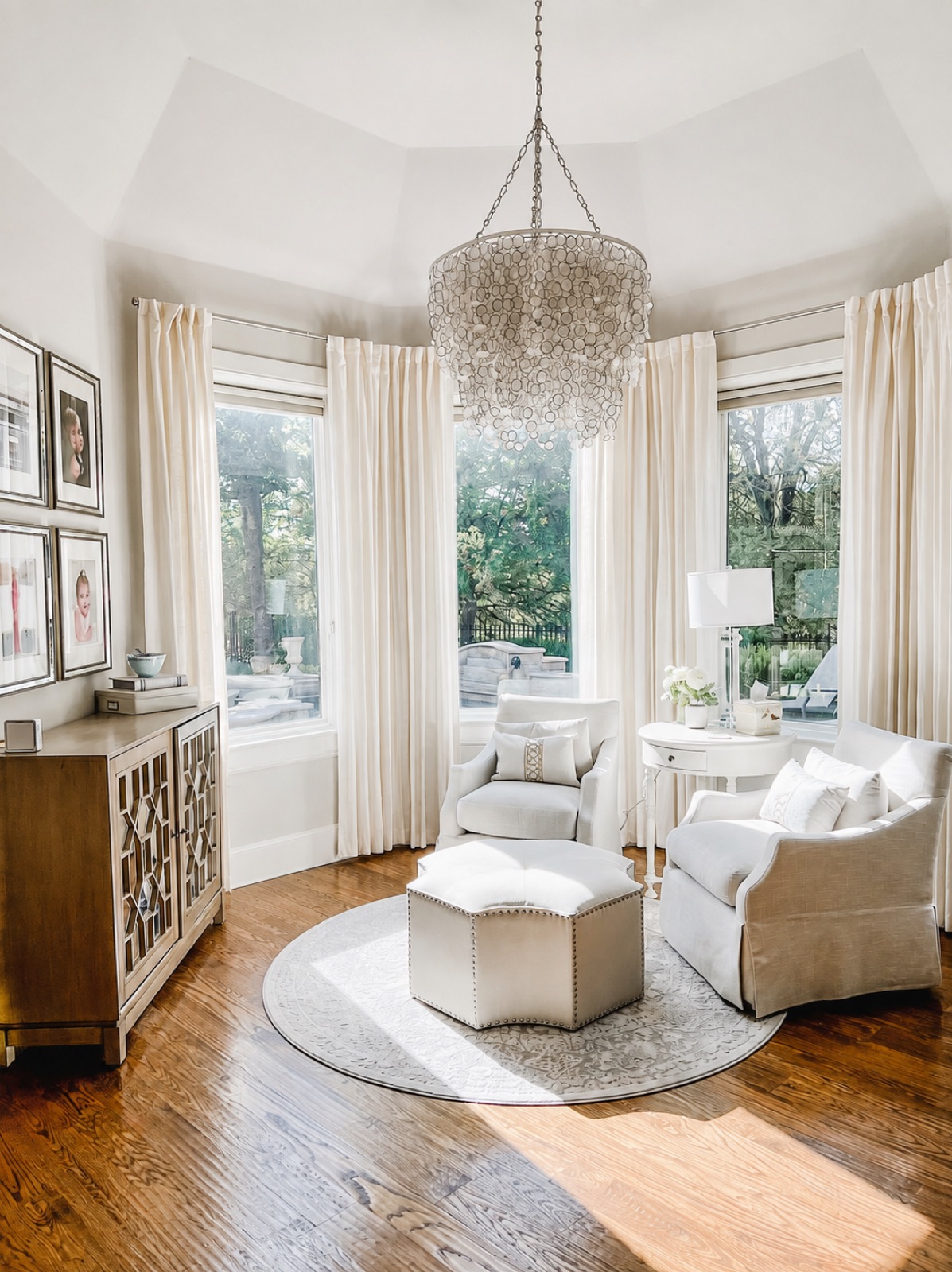 Sitting room with bay window, capiz shell chandelier, and cream slipcovered chairs